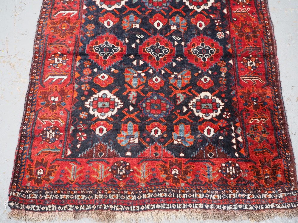 An antique hand-knotted Persian Shiraz wool rug featuring geometric tribal medallions in red, dark blue, and ivory. View IV