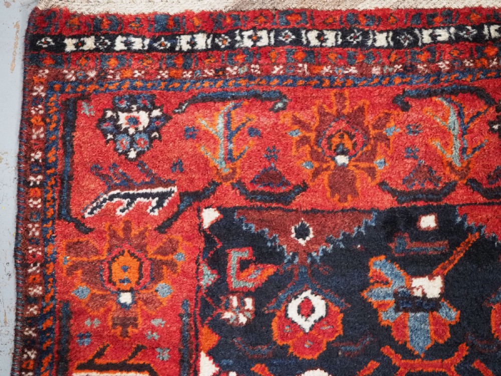 An antique hand-knotted Persian Shiraz wool rug featuring geometric tribal medallions in red, dark blue, and ivory. View V