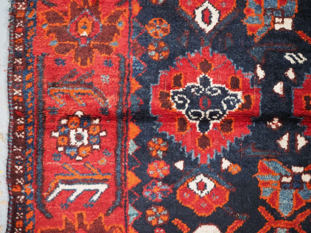 An antique hand-knotted Persian Shiraz wool rug featuring geometric tribal medallions in red, dark blue, and ivory. View VI