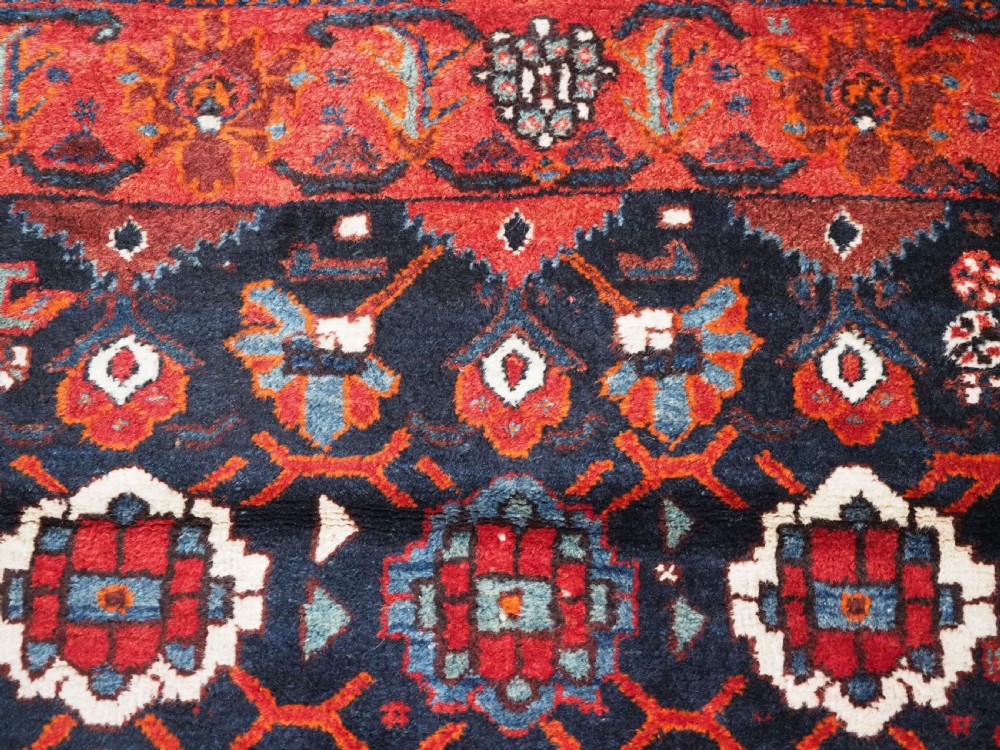 An antique hand-knotted Persian Shiraz wool rug featuring geometric tribal medallions in red, dark blue, and ivory. View VII
