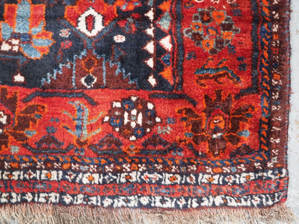 An antique hand-knotted Persian Shiraz wool rug featuring geometric tribal medallions in red, dark blue, and ivory. View X