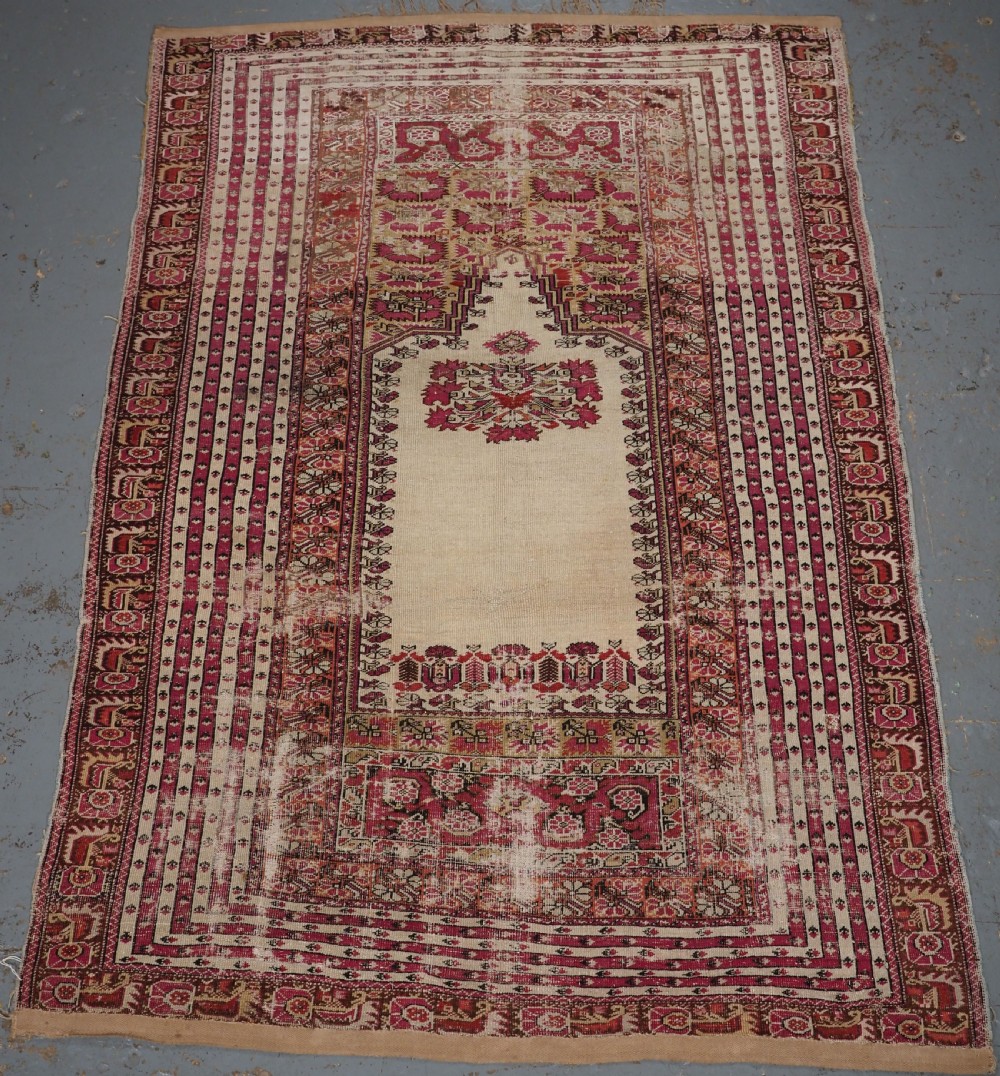 An antique Turkish Ghiordes prayer rug featuring a cream central niche framed by multi-banded red and burgundy patterned borders.
