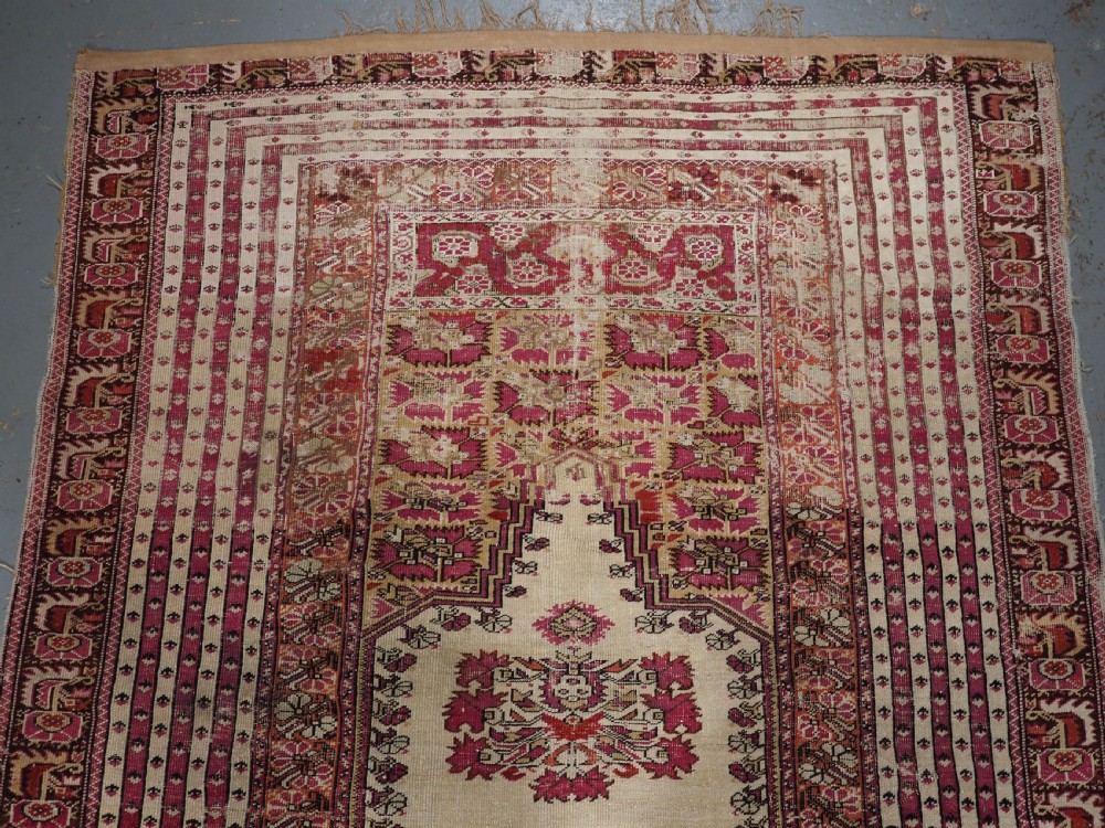 An antique Turkish Ghiordes prayer rug featuring a cream central niche framed by multi-banded red and burgundy patterned borders. View III