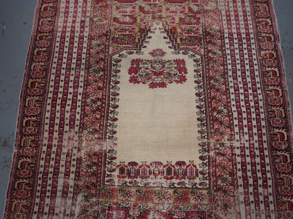 An antique Turkish Ghiordes prayer rug featuring a cream central niche framed by multi-banded red and burgundy patterned borders. View IV
