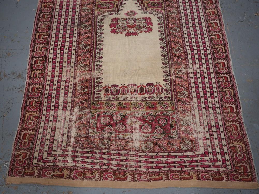 An antique Turkish Ghiordes prayer rug featuring a cream central niche framed by multi-banded red and burgundy patterned borders. View V
