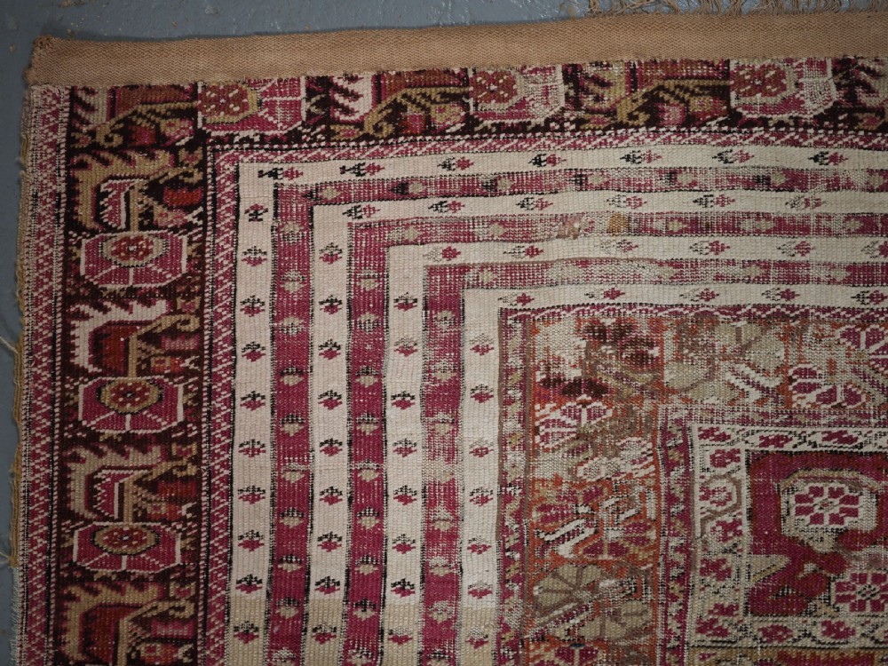 An antique Turkish Ghiordes prayer rug featuring a cream central niche framed by multi-banded red and burgundy patterned borders. View VI