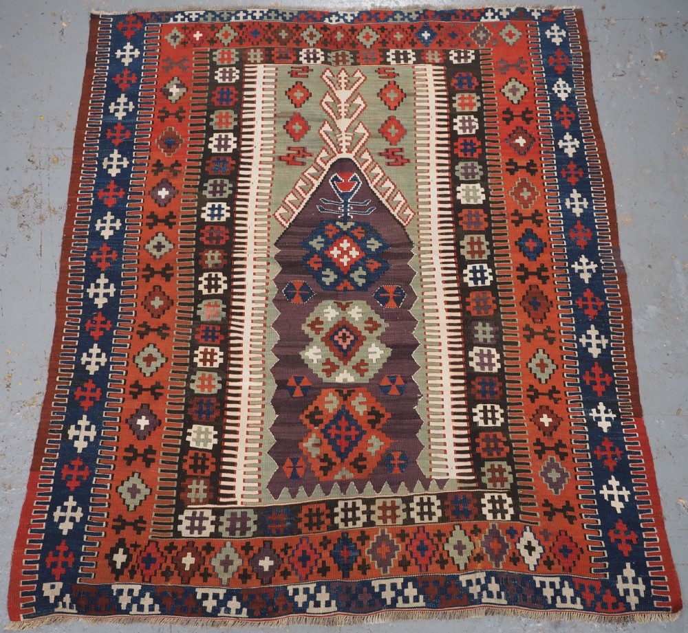 An antique handwoven Turkish Obruk kilim rug featuring a central mihrab niche motif surrounded by geometric borders in terracotta red, dark blue, green, and dark brown.