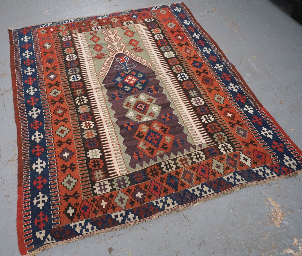 An antique handwoven Turkish Obruk kilim rug featuring a central mihrab niche motif surrounded by geometric borders in terracotta red, dark blue, green, and dark brown. View II