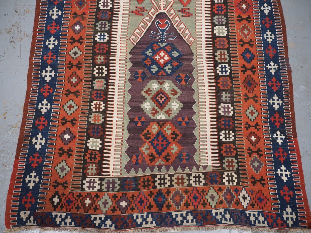 An antique handwoven Turkish Obruk kilim rug featuring a central mihrab niche motif surrounded by geometric borders in terracotta red, dark blue, green, and dark brown. View V