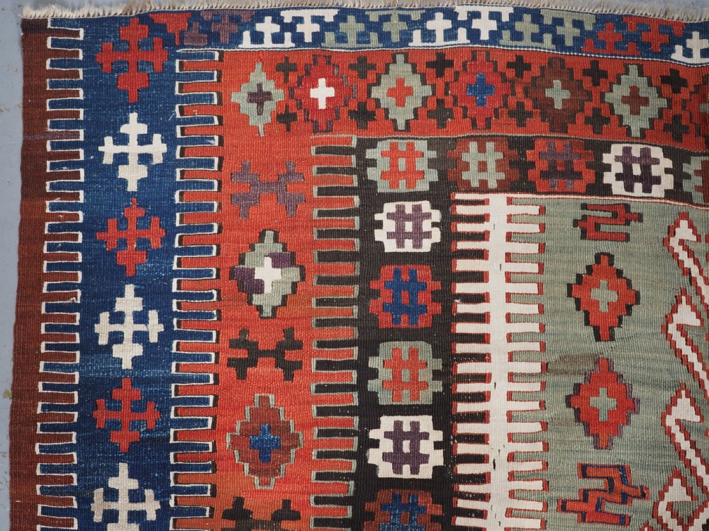 An antique handwoven Turkish Obruk kilim rug featuring a central mihrab niche motif surrounded by geometric borders in terracotta red, dark blue, green, and dark brown. View VI