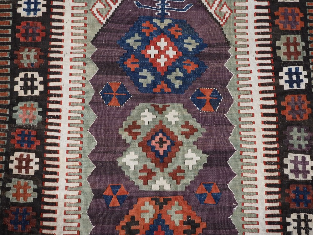 An antique handwoven Turkish Obruk kilim rug featuring a central mihrab niche motif surrounded by geometric borders in terracotta red, dark blue, green, and dark brown. View X