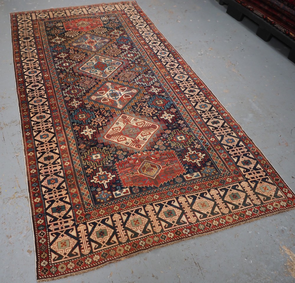 An antique late 19th-century Caucasian Shirvan hand-knotted wool rug featuring geometric diamond medallions, multi-coloured tribal motifs, and a distinct Kufic border. View II