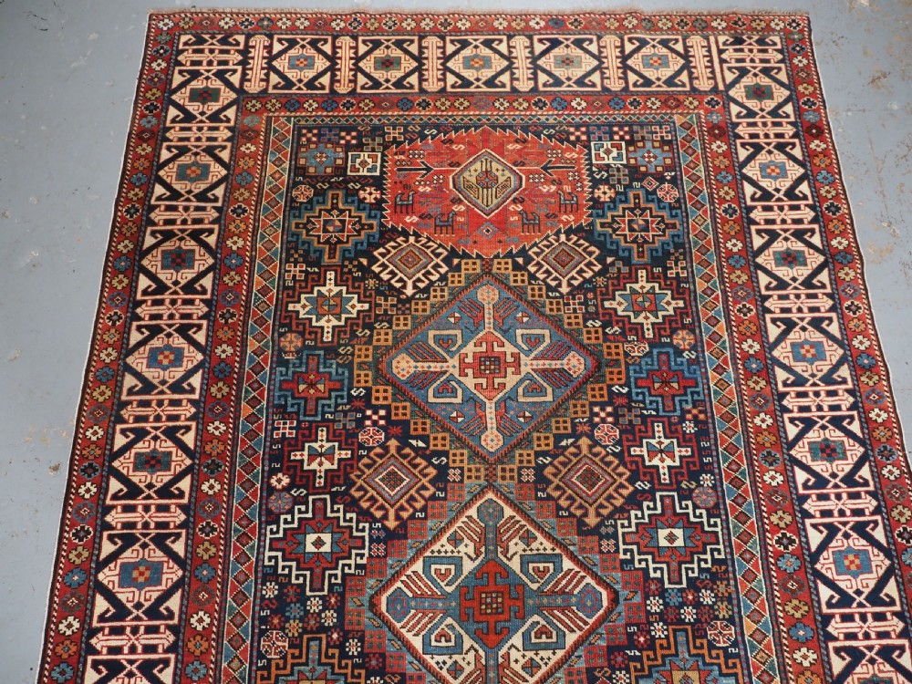 An antique late 19th-century Caucasian Shirvan hand-knotted wool rug featuring geometric diamond medallions, multi-coloured tribal motifs, and a distinct Kufic border. View III