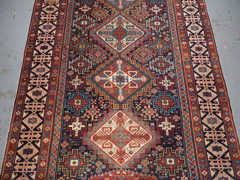 An antique late 19th-century Caucasian Shirvan hand-knotted wool rug featuring geometric diamond medallions, multi-coloured tribal motifs, and a distinct Kufic border. View IV