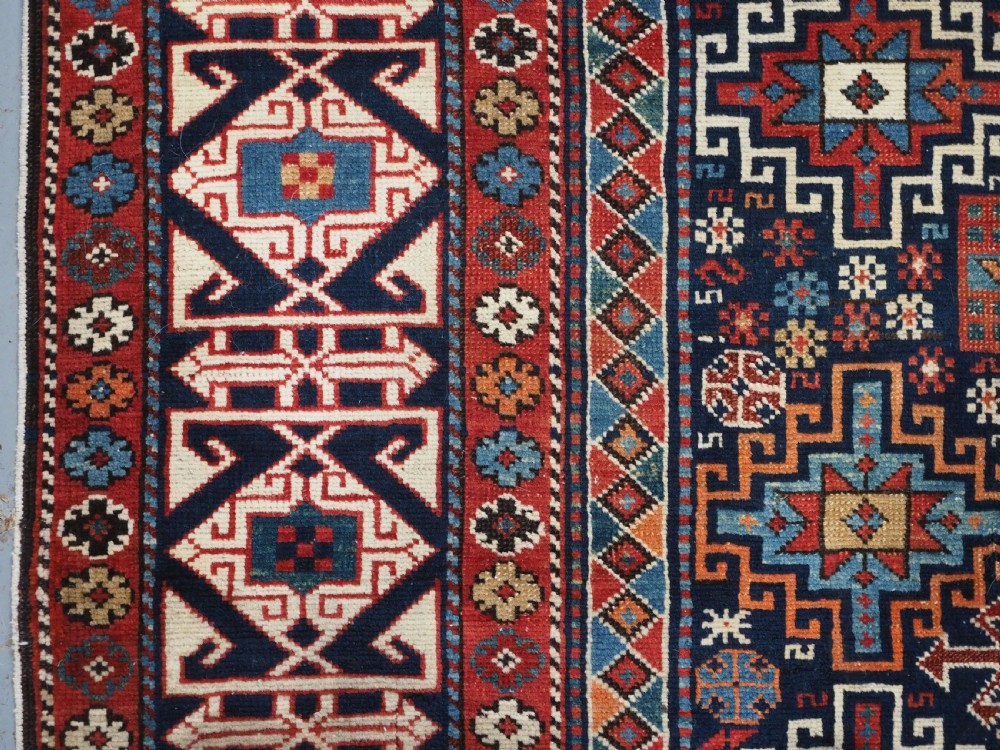 An antique late 19th-century Caucasian Shirvan hand-knotted wool rug featuring geometric diamond medallions, multi-coloured tribal motifs, and a distinct Kufic border. View VII