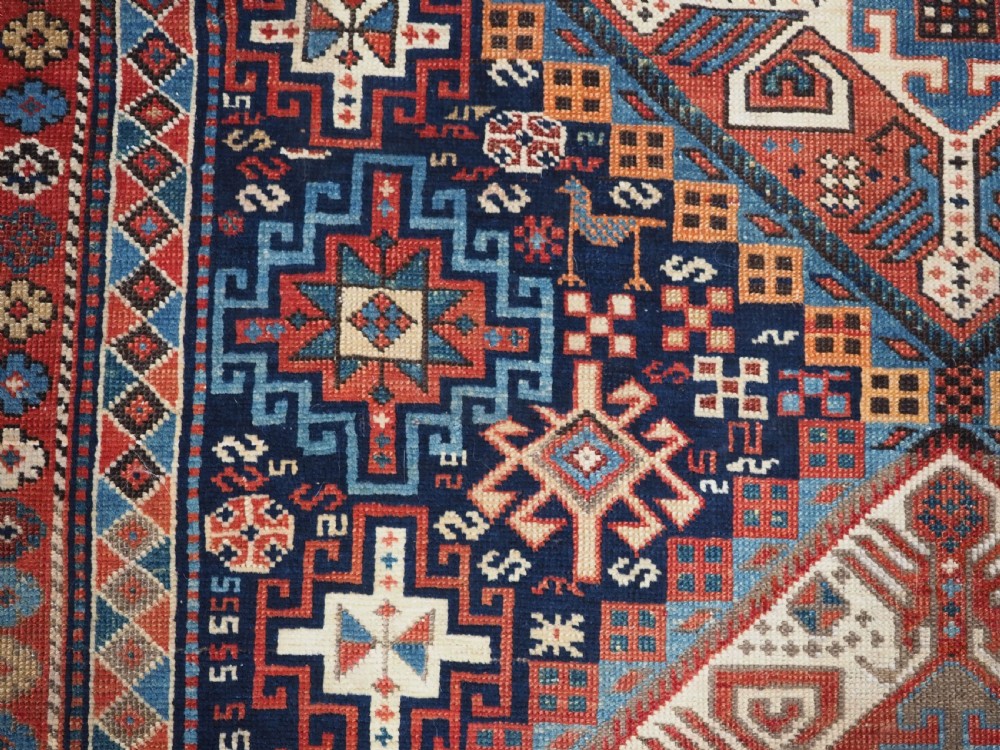 An antique late 19th-century Caucasian Shirvan hand-knotted wool rug featuring geometric diamond medallions, multi-coloured tribal motifs, and a distinct Kufic border. View XV