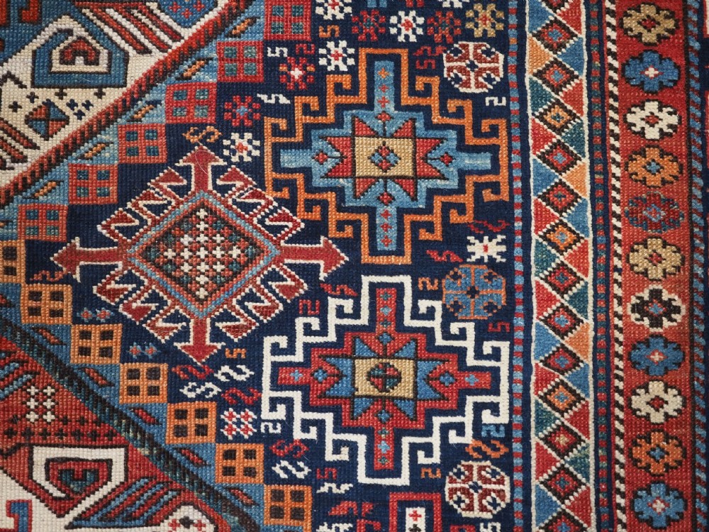 An antique late 19th-century Caucasian Shirvan hand-knotted wool rug featuring geometric diamond medallions, multi-coloured tribal motifs, and a distinct Kufic border. View XVI