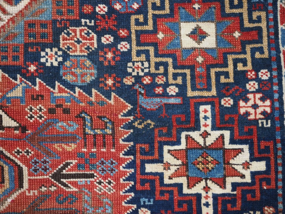 An antique late 19th-century Caucasian Shirvan hand-knotted wool rug featuring geometric diamond medallions, multi-coloured tribal motifs, and a distinct Kufic border. View XVII