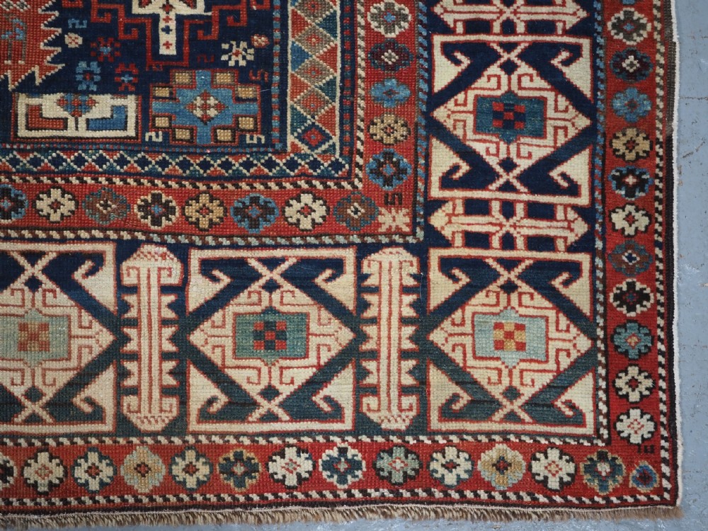 An antique late 19th-century Caucasian Shirvan hand-knotted wool rug featuring geometric diamond medallions, multi-coloured tribal motifs, and a distinct Kufic border. View XVIII