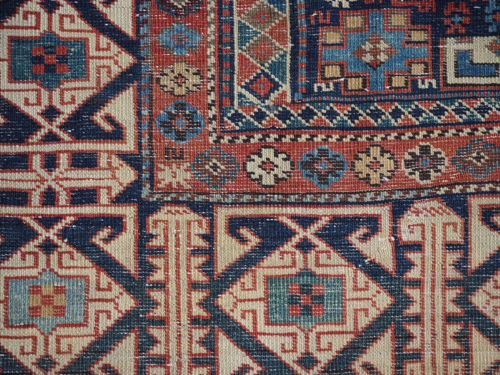 An antique late 19th-century Caucasian Shirvan hand-knotted wool rug featuring geometric diamond medallions, multi-coloured tribal motifs, and a distinct Kufic border. View XIX