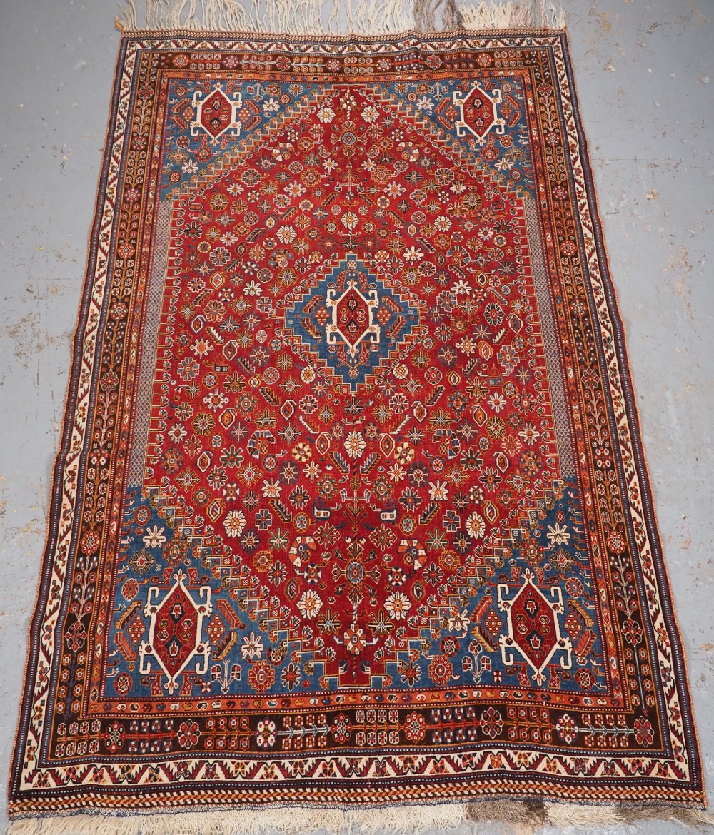 An antique hand-knotted wool Qashqai rug featuring a central stepped medallion surrounded by intricate geometric motifs in shades of terracotta red, indigo blue, and ivory.