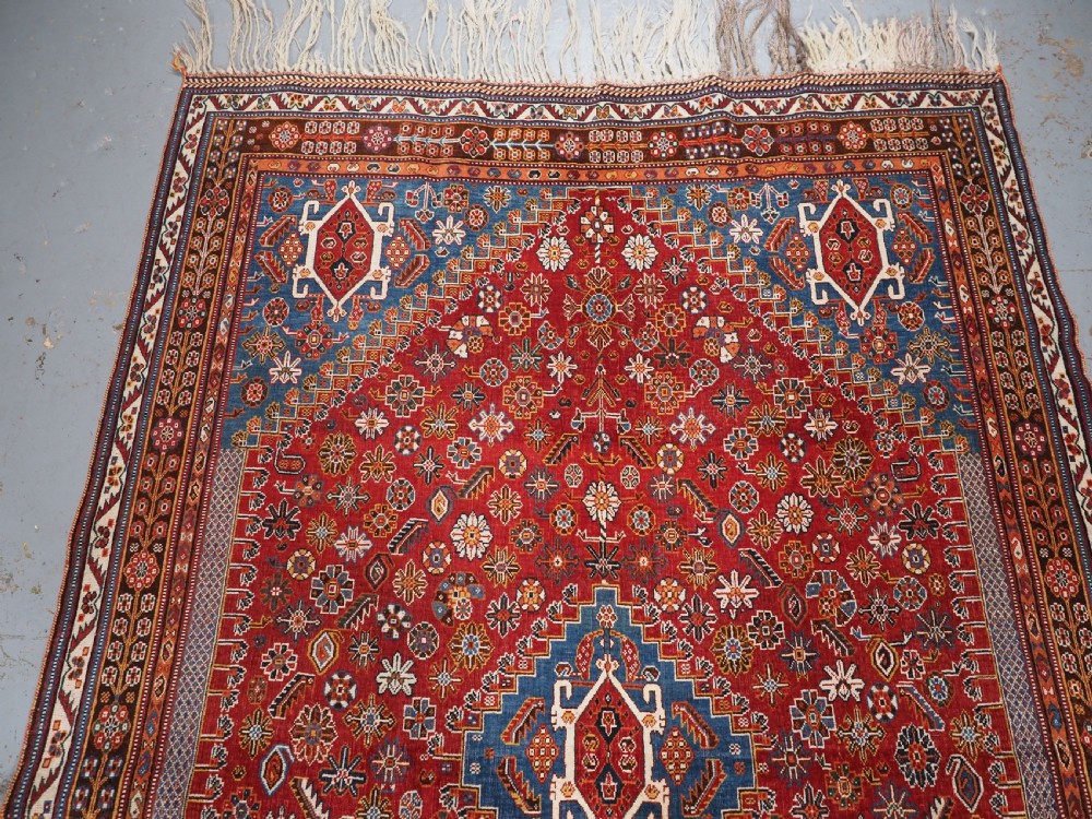 An antique hand-knotted wool Qashqai rug featuring a central stepped medallion surrounded by intricate geometric motifs in shades of terracotta red, indigo blue, and ivory. View III