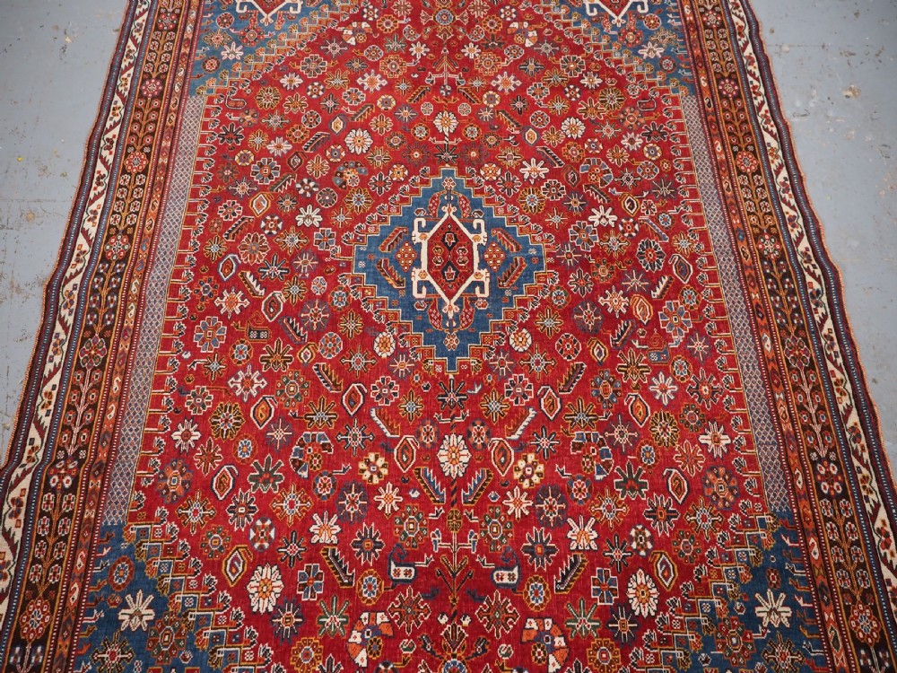 An antique hand-knotted wool Qashqai rug featuring a central stepped medallion surrounded by intricate geometric motifs in shades of terracotta red, indigo blue, and ivory. View IV