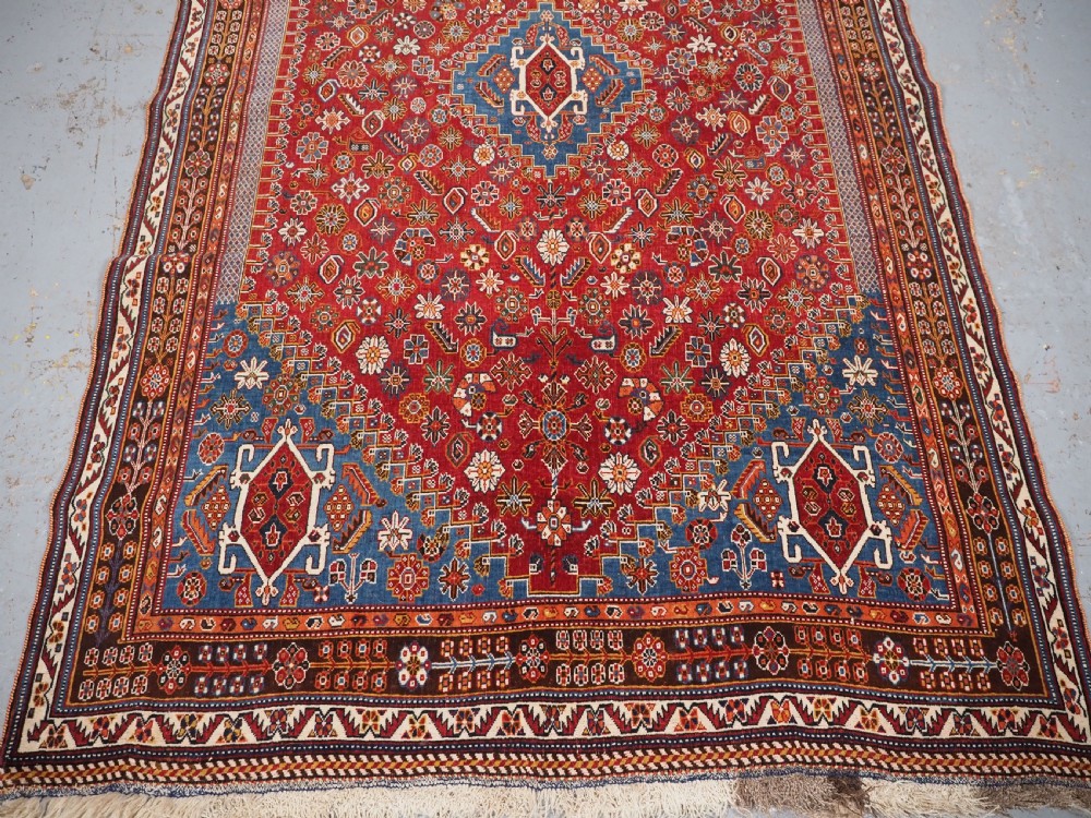 An antique hand-knotted wool Qashqai rug featuring a central stepped medallion surrounded by intricate geometric motifs in shades of terracotta red, indigo blue, and ivory. View V