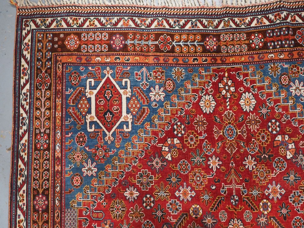 An antique hand-knotted wool Qashqai rug featuring a central stepped medallion surrounded by intricate geometric motifs in shades of terracotta red, indigo blue, and ivory. View VI