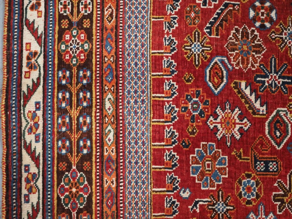 An antique hand-knotted wool Qashqai rug featuring a central stepped medallion surrounded by intricate geometric motifs in shades of terracotta red, indigo blue, and ivory. View VII