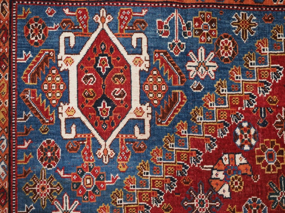 An antique hand-knotted wool Qashqai rug featuring a central stepped medallion surrounded by intricate geometric motifs in shades of terracotta red, indigo blue, and ivory. View VIII