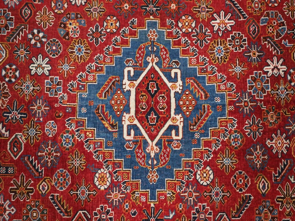 An antique hand-knotted wool Qashqai rug featuring a central stepped medallion surrounded by intricate geometric motifs in shades of terracotta red, indigo blue, and ivory. View X