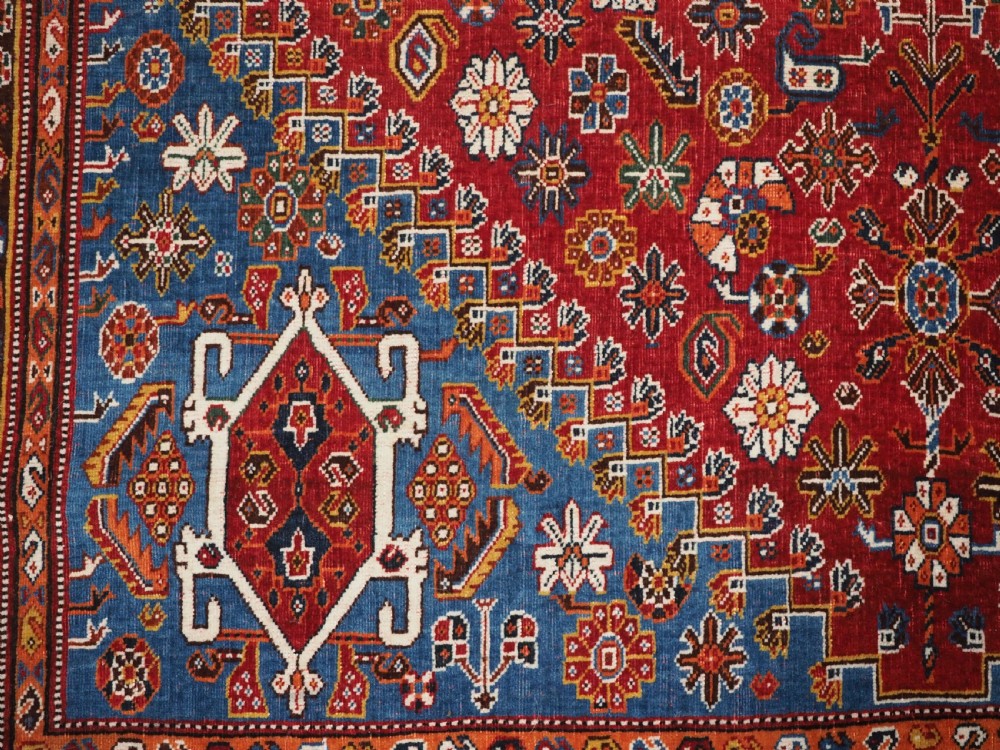 An antique hand-knotted wool Qashqai rug featuring a central stepped medallion surrounded by intricate geometric motifs in shades of terracotta red, indigo blue, and ivory. View XII