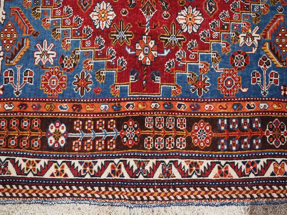 An antique hand-knotted wool Qashqai rug featuring a central stepped medallion surrounded by intricate geometric motifs in shades of terracotta red, indigo blue, and ivory. View XIII