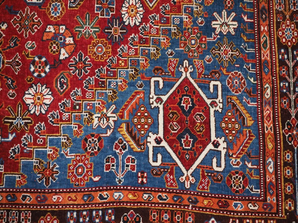 An antique hand-knotted wool Qashqai rug featuring a central stepped medallion surrounded by intricate geometric motifs in shades of terracotta red, indigo blue, and ivory. View XIV