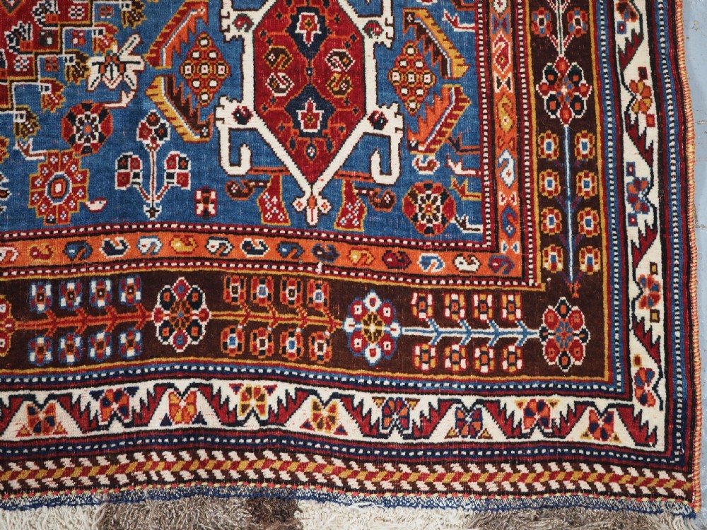 An antique hand-knotted wool Qashqai rug featuring a central stepped medallion surrounded by intricate geometric motifs in shades of terracotta red, indigo blue, and ivory. View XV