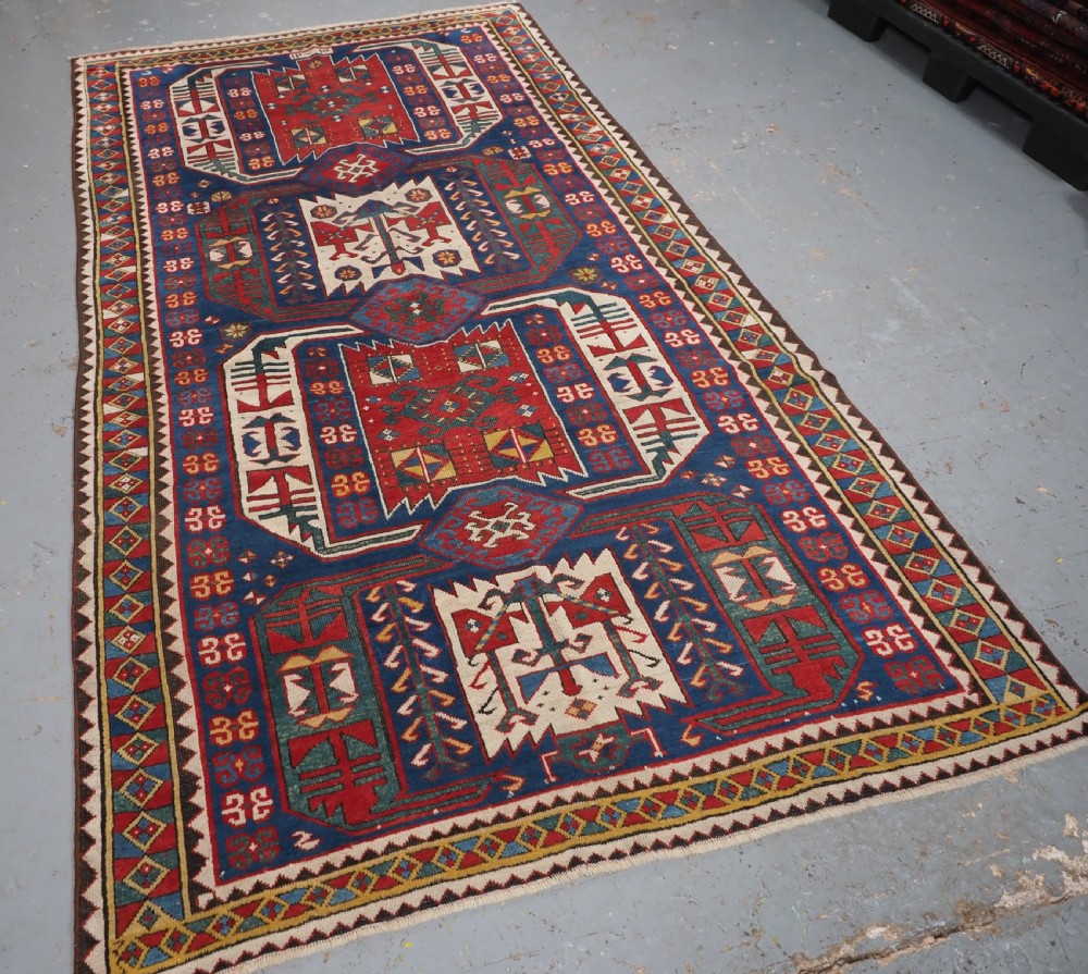 An antique hand-knotted Caucasian Kasim-Usag wool rug featuring geometric red and ivory medallions set on a dark navy blue field with multi-coloured geometric borders. View II