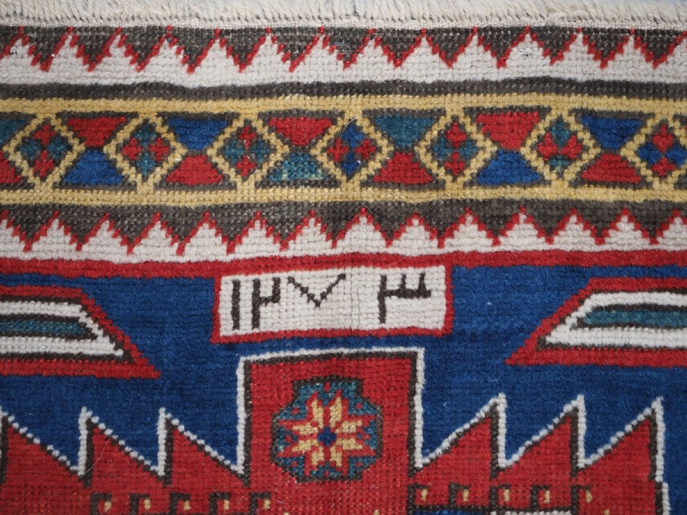 An antique hand-knotted Caucasian Kasim-Usag wool rug featuring geometric red and ivory medallions set on a dark navy blue field with multi-coloured geometric borders. View VIII