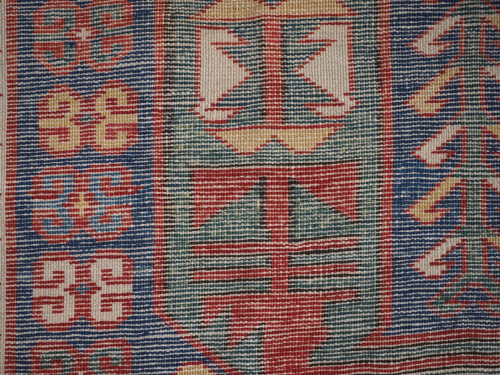 An antique hand-knotted Caucasian Kasim-Usag wool rug featuring geometric red and ivory medallions set on a dark navy blue field with multi-coloured geometric borders. View XV