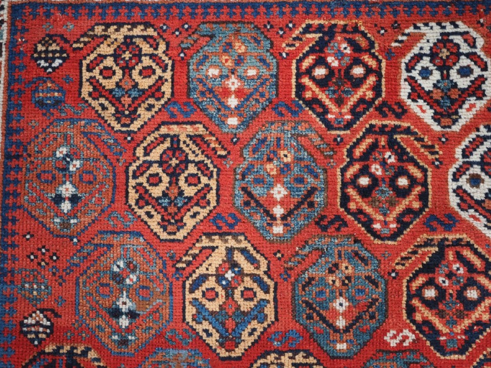 An antique hand-knotted wool rug featuring a deep red field filled with repeating geometric boteh patterns framed by dark blue geometric borders. View VIII