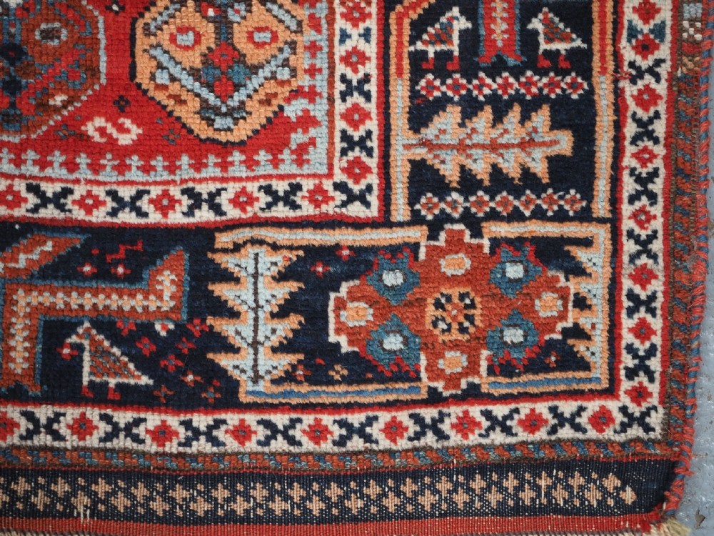 An antique hand-knotted wool rug featuring a deep red field filled with repeating geometric boteh patterns framed by dark blue geometric borders. View XII