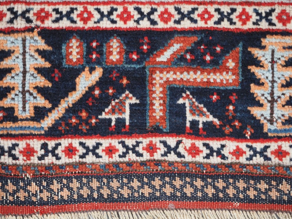 An antique hand-knotted wool rug featuring a deep red field filled with repeating geometric boteh patterns framed by dark blue geometric borders. View XIII