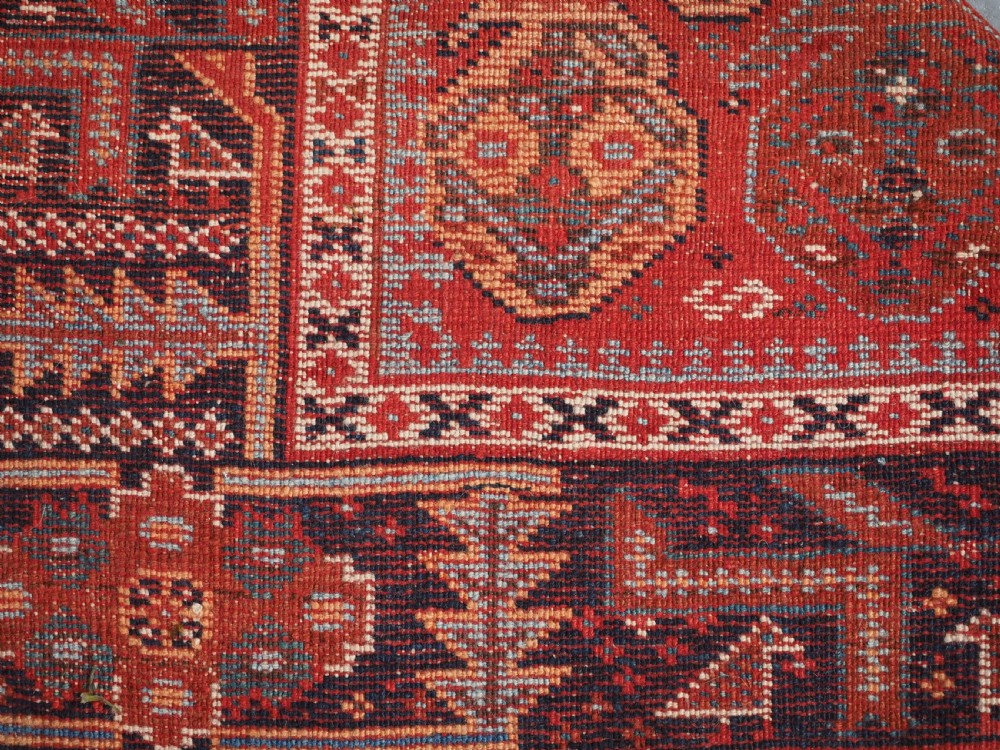 An antique hand-knotted wool rug featuring a deep red field filled with repeating geometric boteh patterns framed by dark blue geometric borders. View XIV