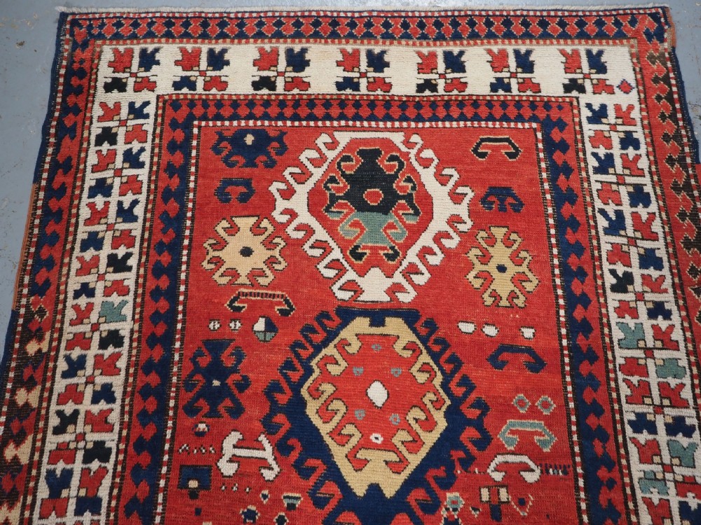 An antique Caucasian Bordjalou Kazak hand-knotted wool rug featuring three stepped geometric medallions on a vibrant red field within patterned borders. View III