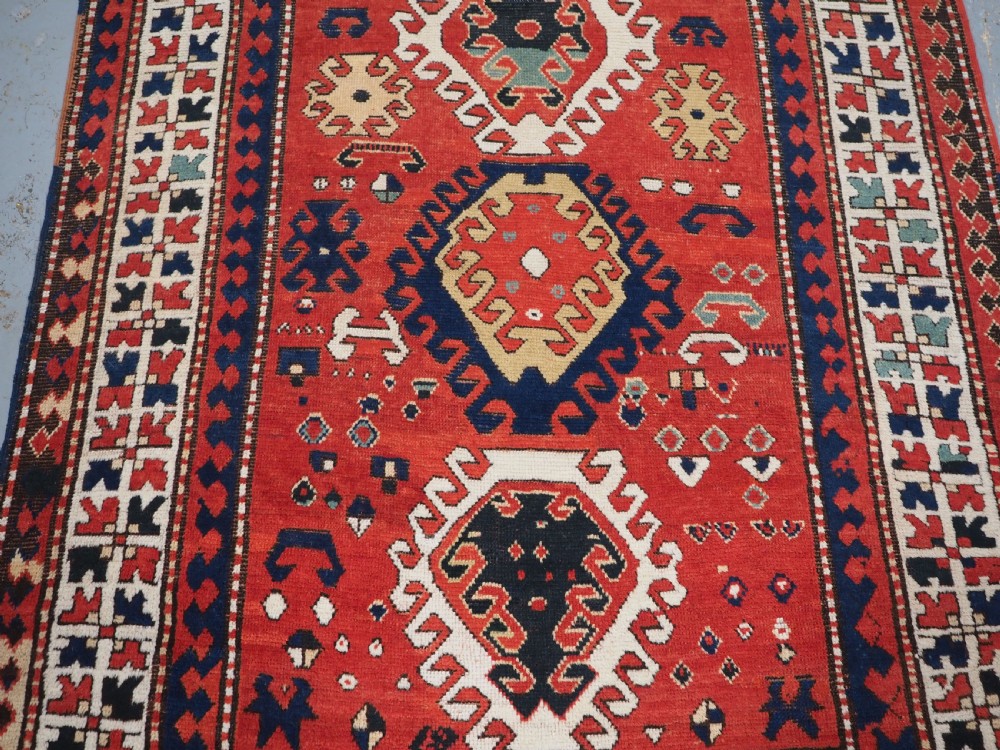 An antique Caucasian Bordjalou Kazak hand-knotted wool rug featuring three stepped geometric medallions on a vibrant red field within patterned borders. View IV