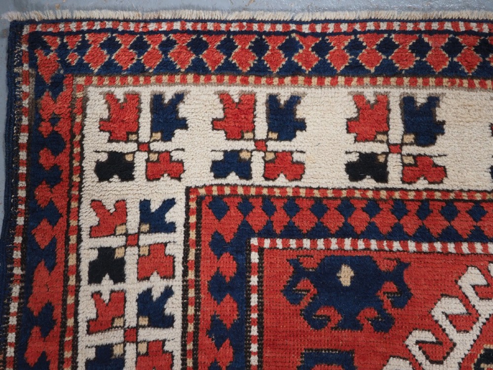 An antique Caucasian Bordjalou Kazak hand-knotted wool rug featuring three stepped geometric medallions on a vibrant red field within patterned borders. View VI