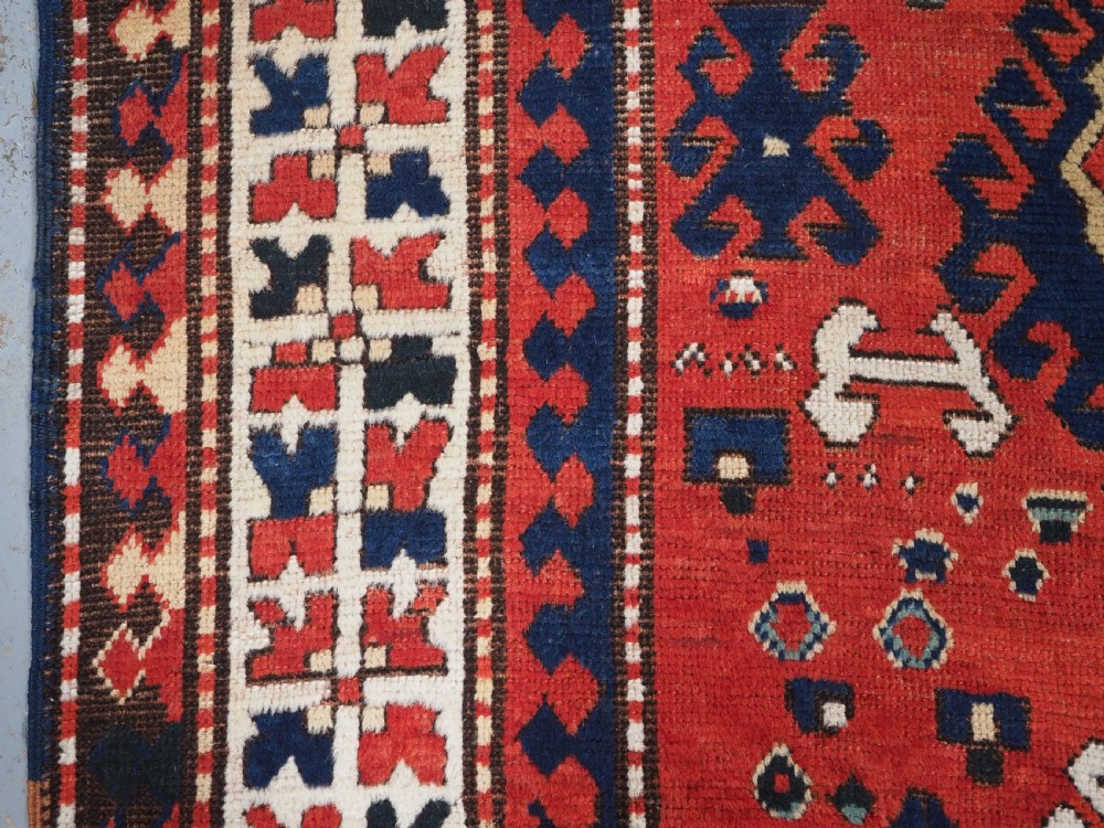 An antique Caucasian Bordjalou Kazak hand-knotted wool rug featuring three stepped geometric medallions on a vibrant red field within patterned borders. View VII