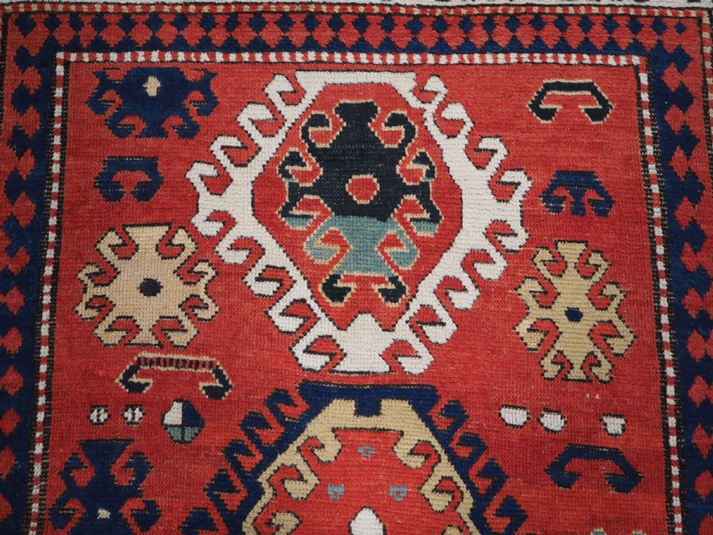 An antique Caucasian Bordjalou Kazak hand-knotted wool rug featuring three stepped geometric medallions on a vibrant red field within patterned borders. View VIII
