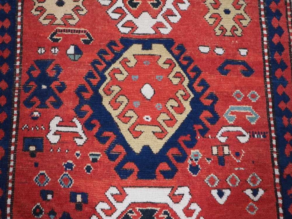 An antique Caucasian Bordjalou Kazak hand-knotted wool rug featuring three stepped geometric medallions on a vibrant red field within patterned borders. View IX