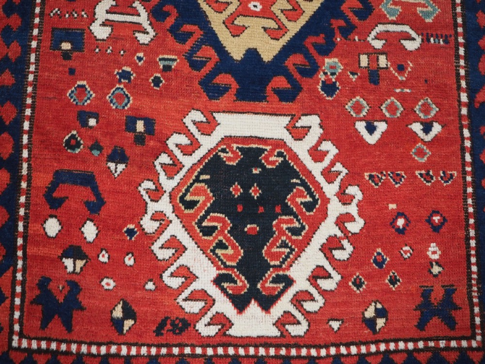 An antique Caucasian Bordjalou Kazak hand-knotted wool rug featuring three stepped geometric medallions on a vibrant red field within patterned borders. View X